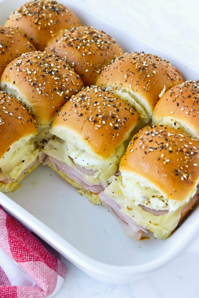 Closeup of breakfast sliders in a baking dish. Three sliders removed to show filling of sliders.