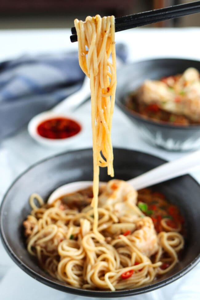 Chopsticks pulling noodles from a bowl of soup noodles.