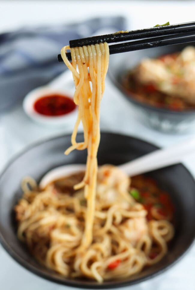 Chopsticks pulling dan dan noodles from a bowl.