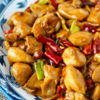 Closeup front view of plate with chicken stir-fry. Text overlay "Authentic Kung Pao Chicken" and "thatspicychick.com.