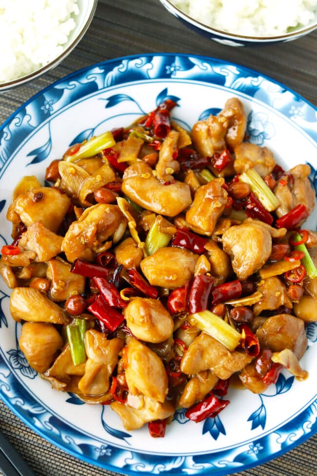 Top view of spicy chicken stir-fry on a plate and two bowls with rice.
