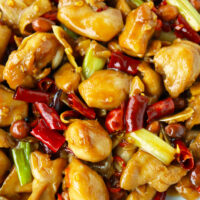 Closeup of spicy chicken stir-fry. Text overlay "The Best Kung Pao Chicken" and "thatspicychick.com.