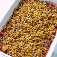 Baked strawberry crisp in a baking dish. Text overlay "Baileys Strawberries & Cream Strawberry Crisp" and "thatspicychick.com.