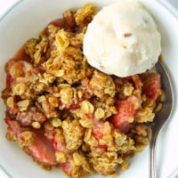 Strawberry crisp in bowl with a spoon and scoop of vanilla pecan ice cream.