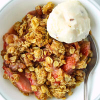 Bowl with strawberry crisp and scoop of ice cream. Text overlay "Baileys Strawberries & Cream Strawberry Crisp" and "thatspicychick.com.