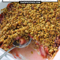 Baking dish with a serving of strawberry crisp out to show inside. Text overlay "Strawberry Crisp with Baileys Strawberries & Cream", and "thatspicychick.com!.