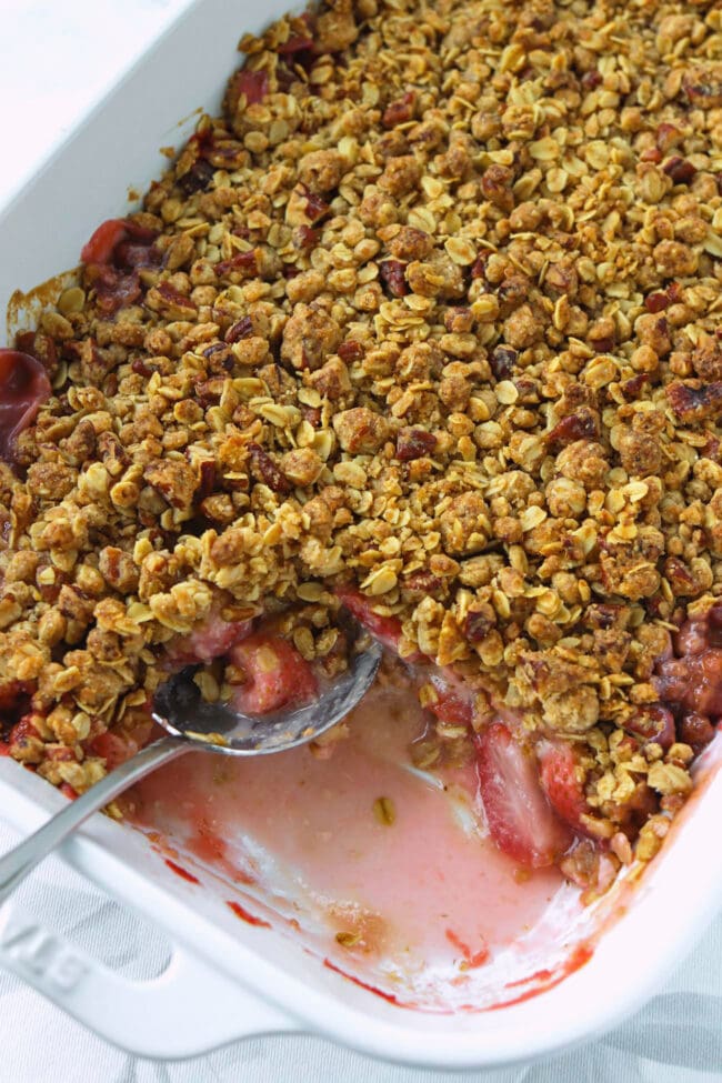 Baking dish with strawberry crisp with a serving taken out to show the inside.