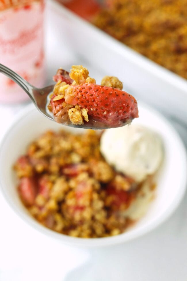 Spoon holding up a bite of strawberry crisp above bowl.