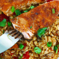 Closeup of fish on bed of rice being flaked by a fork. Text overlay "Thai Chili Jam Salmon & Rice Bake" and "thatspicychick.com".