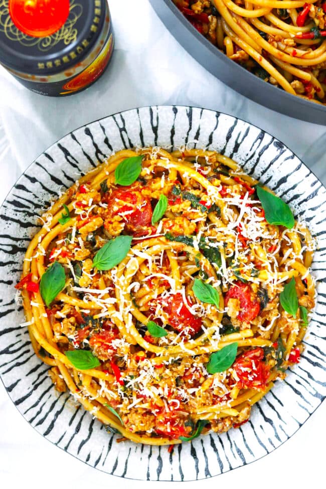 Burst cherry tomato and ground pork pasta dish on a plate and in a pan.