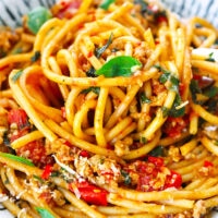 Closeup of bucatini and cherry tomatoes pasta pile on a plate. Text overlay "XO Sauce Pasta with Pork & Burst Cherry Tomatoes" and "thatspicychick.com".