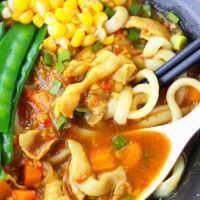 Spoon and chopsticks in a bowl with noodle soup. Text overlay "Japanese Curry Udon with Thin Sliced Pork Belly" and "thatspicychick.com".