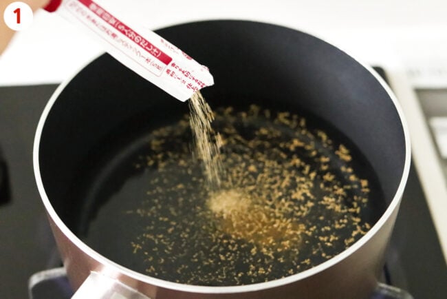 Emptying sachet of dashi powder into pot with water on stovetop.