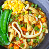 Bowl with soup noodles, sweet corn kernels, and snap peas. Text overlay "Japanese Curry Udon with Thin Sliced Pork Belly" and "thatspicychick.com".