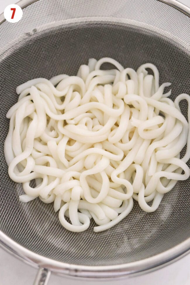 Cooked udon in a fine mesh strainer.