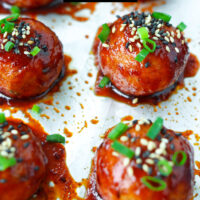 Baked Korean meatballs garnished with spring onion and sesame seeds on a sheet of foil. Text overlay "Spicy Gochujang Chicken Meatballs" and "thatspicychick.com".