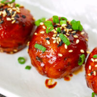 Closeup of gochujang glazed chicken meatball garnished with spring onion and sesame seeds on plate.