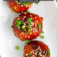 Closeup of plate with Korean meatballs garnished with spring onion and sesame seeds. Text overlay "Spicy Gochujang Chicken Meatballs" and "thatspicychick.com".