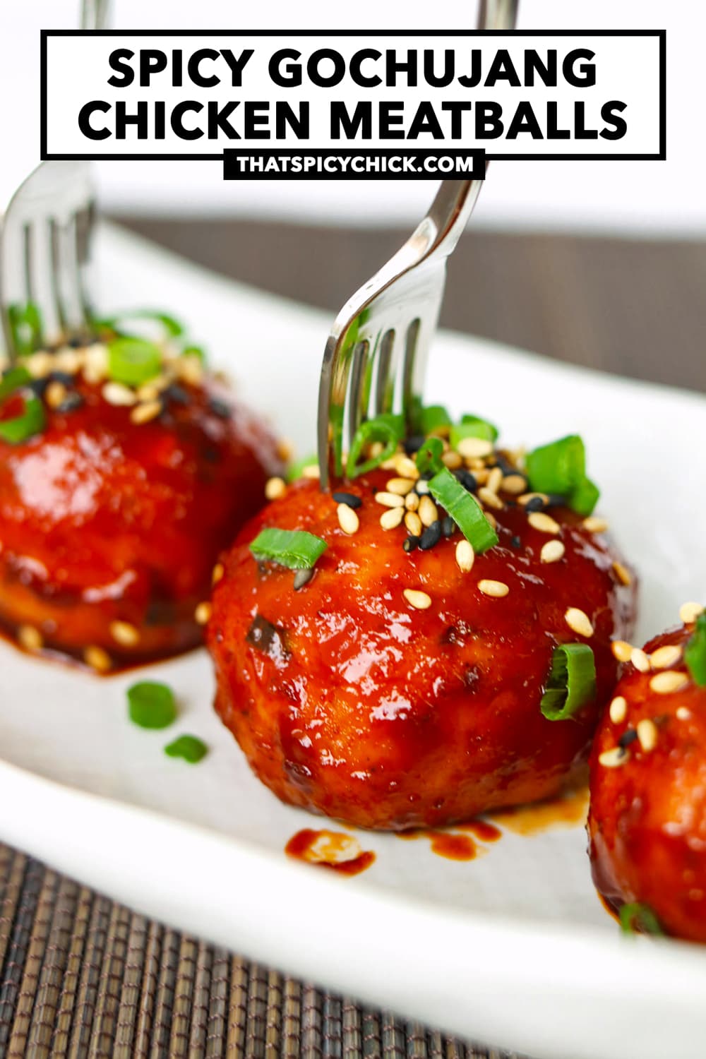 Closeup of meatball with mini fork pierced inside. Text overlay "Spicy Gochujang Chicken Meatballs" and "thatspicychick.com".