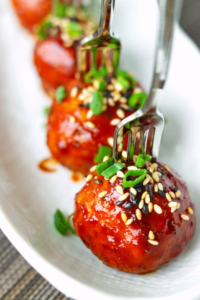 Korean meatballs pierced with mini forks on a long plate.