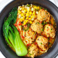 Top view of bowl with soup noodles, meatballs, corn and bok choy. Text overlay "Spicy Miso Ramen with Juicy Chicken Meatballs" and "thatspicychick.com".