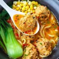Closeup of chicken meatball in a bowl with spicy noodle soup. Text overlay "Spicy Miso Ramen with Juicy Chicken Meatballs" and "thatspicychick.com".