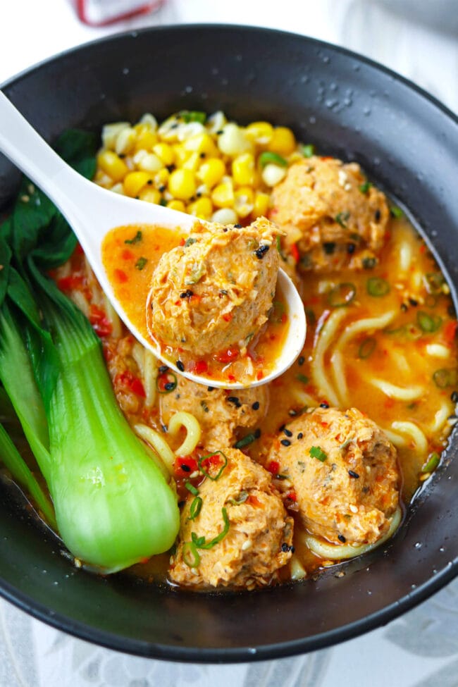 Chicken meatball on a spoon in a bowl of ramen noodle soup.