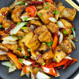 Stir-fried fried fish with red bell pepper and onion on a black plate.