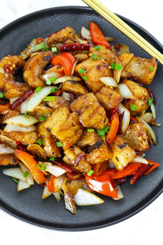Stir-fried fried fish with red bell pepper and onion on a black plate.