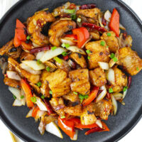 Top view of plate with fried fish stir-fry. Text overlay "Wok Fried Fish in Black Bean Sauce" and "thatspicychick.com".