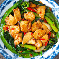 Top view of plate with Chinese chicken and vegetables stir-fry. Text overlay "XO Sauce Chicken & Chinese Broccoli Stir-fry" and "thatspicychick.com".