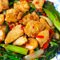 Closeup front view of plate with chicken and Chinese broccoli stir-fry. Text overlay "XO Sauce Chicken & Chinese Broccoli Stir-fry" and "thatspicychick.com".