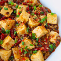 Closeup front view of spicy tofu and pork in a bowl. Text overlay "Braised Tofu & Pork with Pickled Chilies" and "thatspicychick.com".