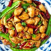 Closeup top view of spicy chicken stir-fry on a plate. Text overlay "Chicken in Vinegar Sauce", "Sichuan Cu Liu Ji", and "thatspicychick.com".