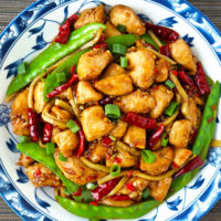 Top view of plate with spicy chicken stir-fry with snow beans and bamboo shoots. Text overlay "Chicken in Vinegar Sauce", "Sichuan Cu Liu Ji", and "thatspicychick.com".