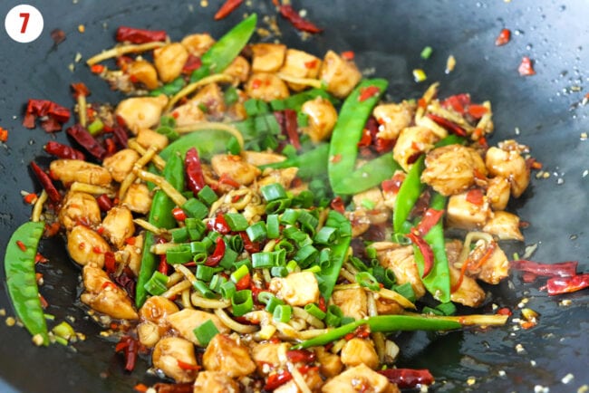 Added spring onion green parts to chicken stir-fry in a wok.