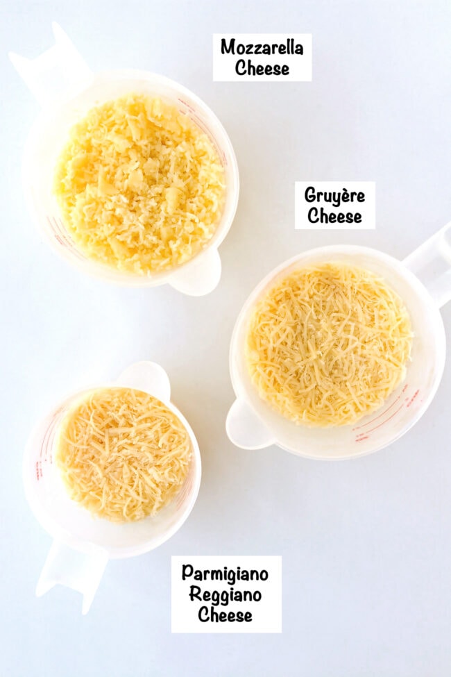 Labeled freshly grated cheeses in measuring cups.