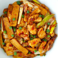 Top view of chicken and tofu stir-fry in a white serving bowl. Text overlay "Spicy Hoisin Chicken & Tofu Stir-fry" and "thatspicychick.com".