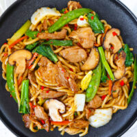Black plate with Chinese pork and vegetables noodles stir-fry.