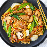 Plate with stir-fried noodles and chopsticks on plate's edge. Text overlay "Shanghai Style Fried Noodles" and "thatspicychick.com".