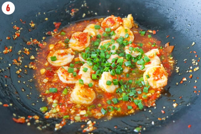 Dry braised shrimp with sauce in a hot wok sprinkled with spring onion.