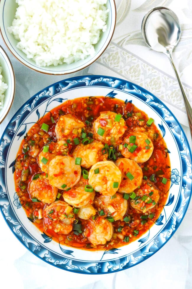 Plate with spicy dry-braised shrimp and rice bowls and a serving spoon.