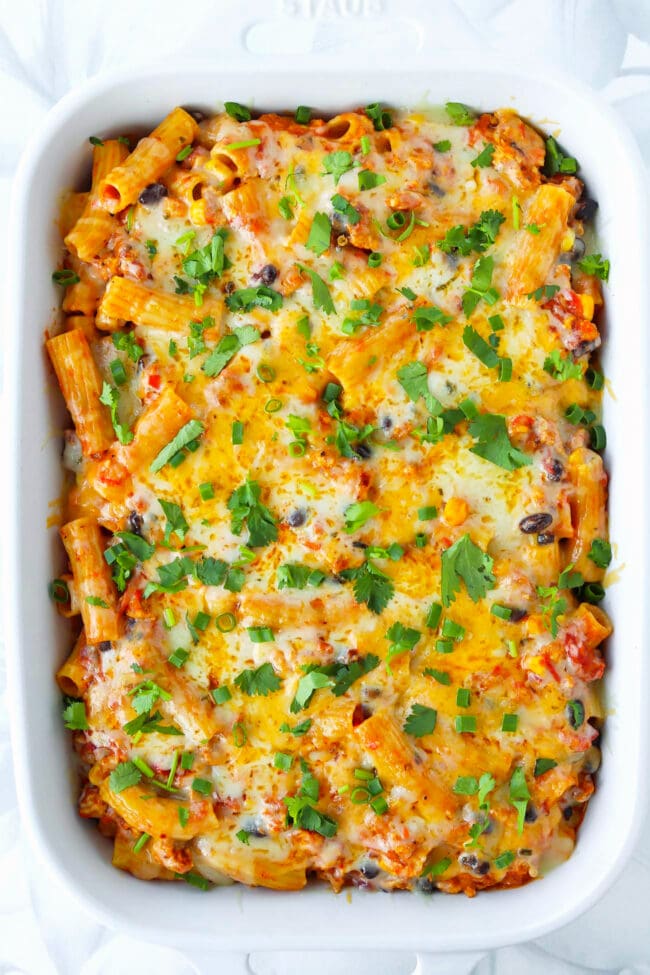 Chicken enchilada pasta with cheesy topping and spring onion and coriander garnish in a baking dish.