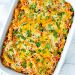 Chicken enchilada pasta with melted cheesy topping in a baking dish.