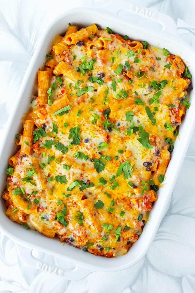 Spicy chicken enchilada pasta bake with melted cheese in a large baking dish.