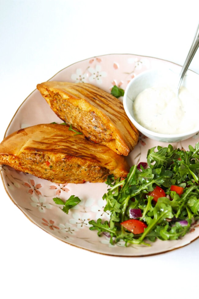 Front view of chicken and lamb arayes on plate with salad and garlic sauce.