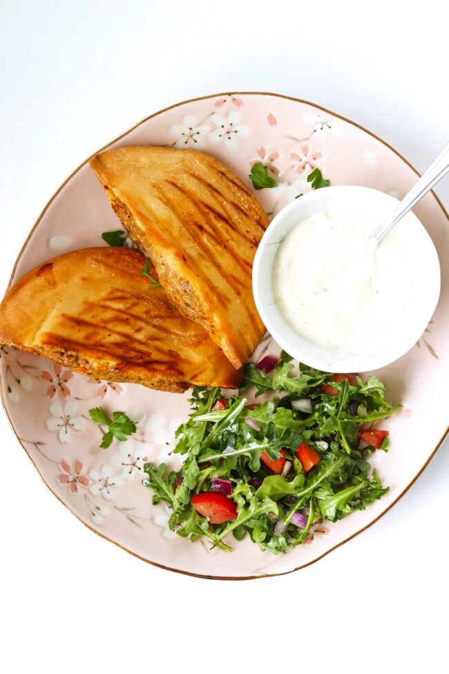 Chicken and lamb arayes on plate with arugula salad and garlic sauce in a bowl.