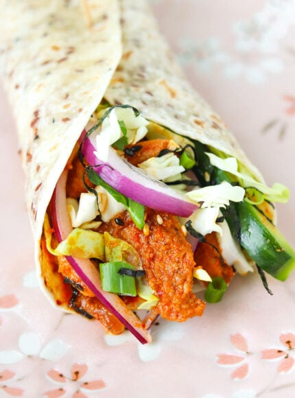 Closeup of gochujang chicken tortilla wrap with veggies, herbs, shredded seaweed, and toasted sesame seeds.