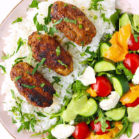 Plate with kofta over steamed rice and salad topped with sauces. Text overlay "Spicy Kofta with Lamb and Chicken" and "thatspicychick.com".
