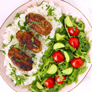 Kofta over steamed rice and salad on a plate.